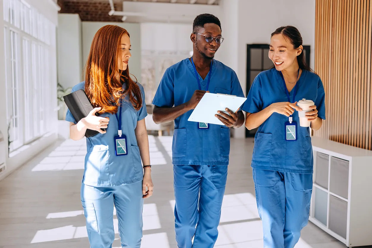 Three nurses in blue scrub smiling and discussing report while walking